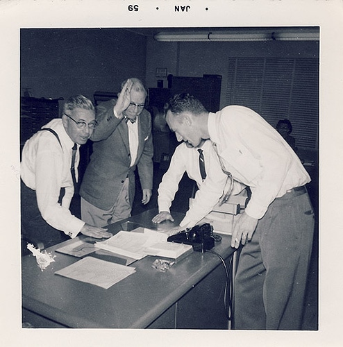 A group of men standing around a table, discussing how to ask for a raise.