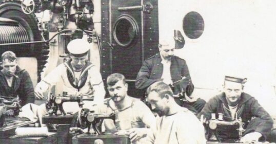A group of men sitting on the floor of a ship, sewing.