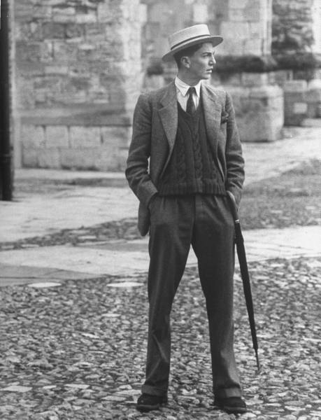 A gentleman in a suit and hat standing on a cobbled street.