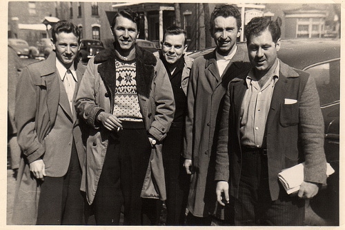 A conflicted group of men standing in front of a modern age car, questioning their manhood.