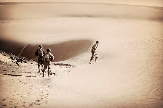 Two people showcasing their masculinity as they walk down a sand dune, captured in a sepia tone.