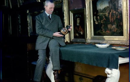 A man in a suit sitting at a table in front of paintings, appearing to invest.