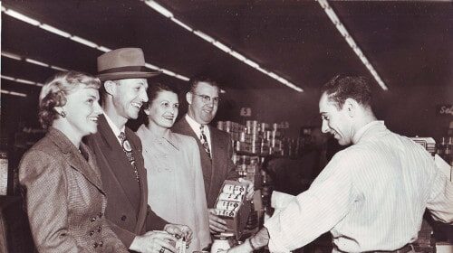 A group of strangers standing at a counter engaged in small talk.