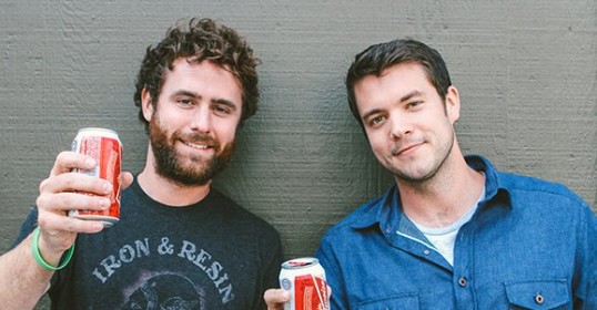 Two men standing next to each other, showcasing the art of manliness as they hold cans of Coca Cola.