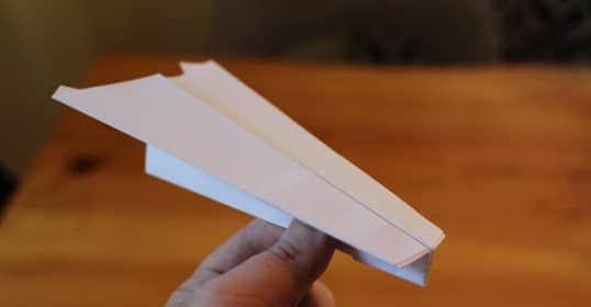 A person showcasing the best paper airplane on a table.