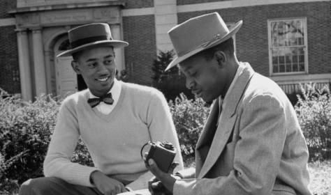 Two men in stylish hats sitting on a bench.