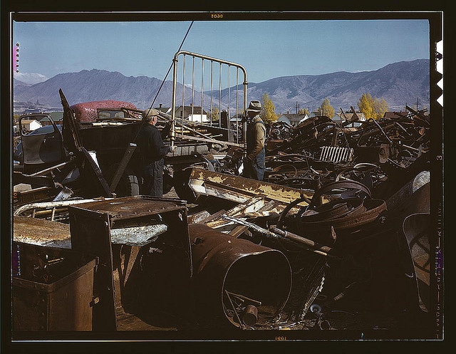 A group of men standing next to a pile of scrap metal, possibly looking to make money.