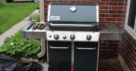 A clean green gas grill with a red bucket beside it.