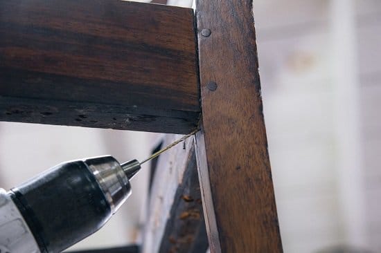 A person is using a drill to repair a common wooden chair.
