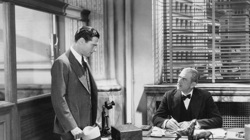 Two men standing at a desk discussing how to fire someone.