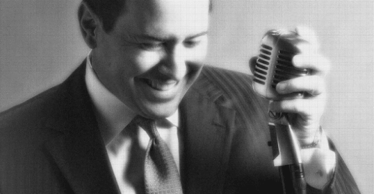 A black and white photo of a man in a suit holding a microphone, hinting at his potential singing career.