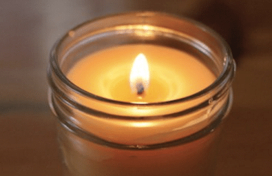 A candle in a mason jar sitting on a wooden table brings a cozy ambience to any room.