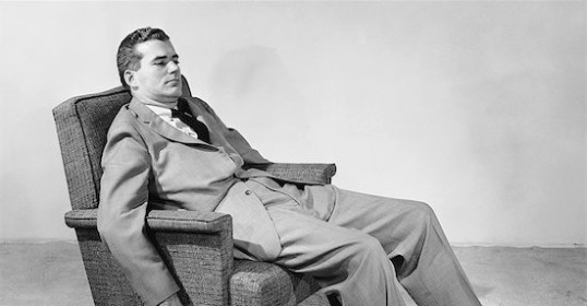 A manliness in a suit sitting in a chair.