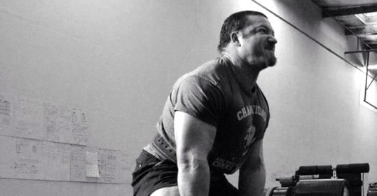 A man is improving his strength by lifting a large barbell in the gym.