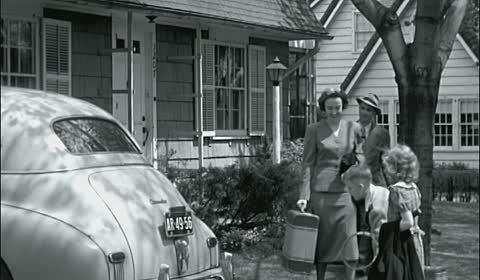 An old black and white photo of a group of people standing near a car on vacation.