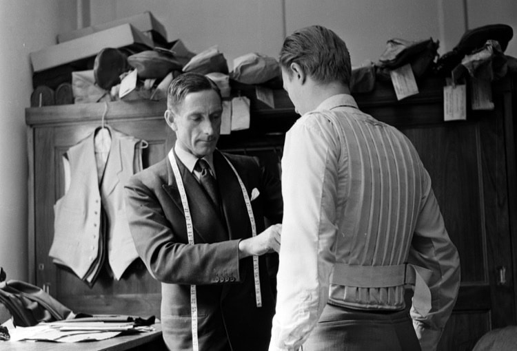 A man in a suit is helping another man find a good tailor.