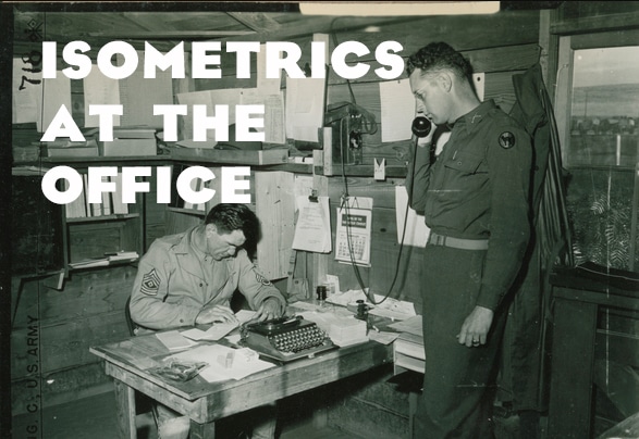 A man in uniform is working at an office desk with another man in uniform.