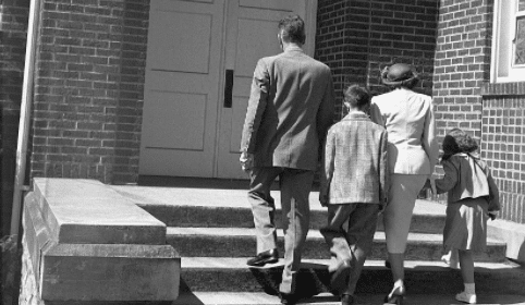 Black and white photo of a family walking down the steps of a church, showcasing their beliefs.
