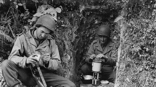 Two WWII soldiers sitting in a cave, enjoying a cup of coffee.