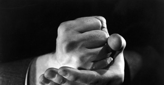 A black and white photo of a man demonstrating his strong willpower with a clenched fist.