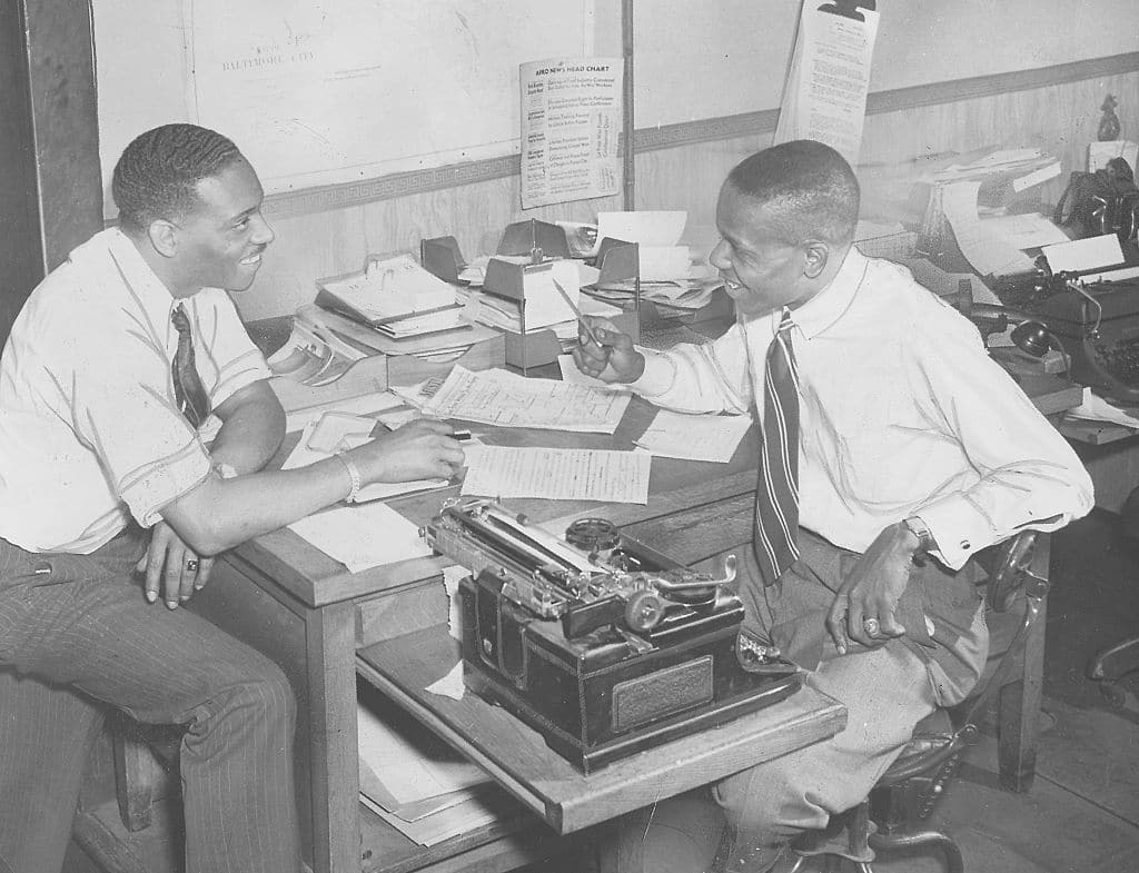 Two entrepreneurs sitting at a desk with a typewriter.