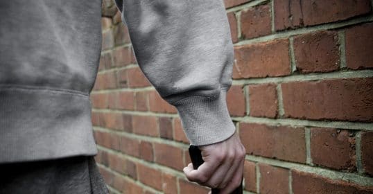 A man brandishing a gun in front of a brick wall, portraying social aggression.