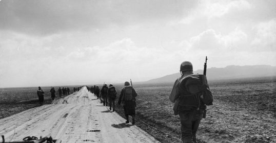 A group of soldiers rucking on a dirt road.