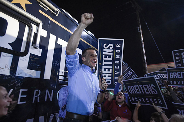 A man, possibly Gov. Eric Greitens, exhibits leadership by holding up signs in front of a crowd.
