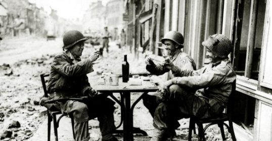 Three soldiers sitting at a table in the ruins, toasting.