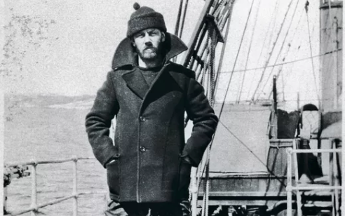 A man in a pea coat standing on the deck of a ship.