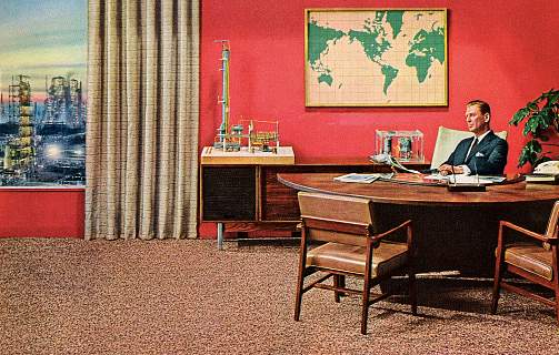 A man at a desk with peers nearby.