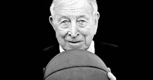 A black and white photo of a legendary coach holding a basketball.