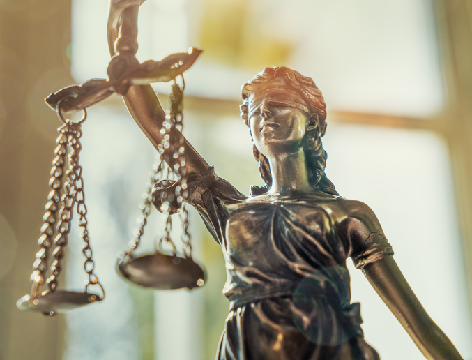 A manvotional statue of justice sitting with scales in front of a window.
