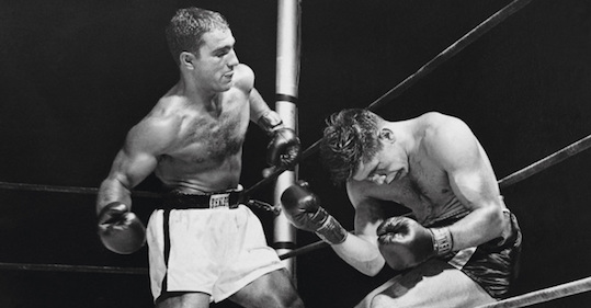 A black and white photograph of two boxers in a boxing ring, captured during a intense fight.