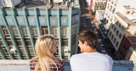 A couple gazes out over the city from the top of a building, feeling romantic attraction.