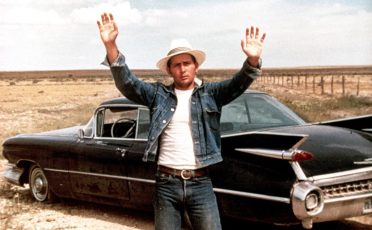 A man in a hat is standing next to a classic car, showcasing his style.