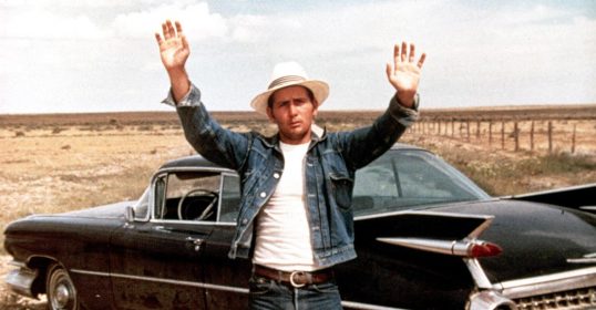 A man in a hat is standing next to a classic car, showcasing his style.