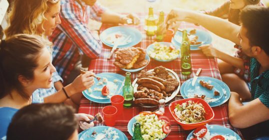 A group of people enjoying a weekend meal at a picnic table hosted by their friend.