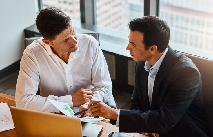 Two bosses discussing at a table in an office.
