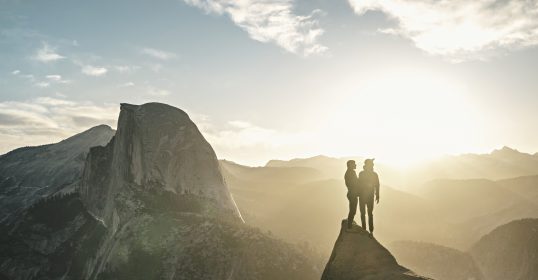 Two people enjoying a happy relationship stand on top of a mountain in Yosemite National Park.