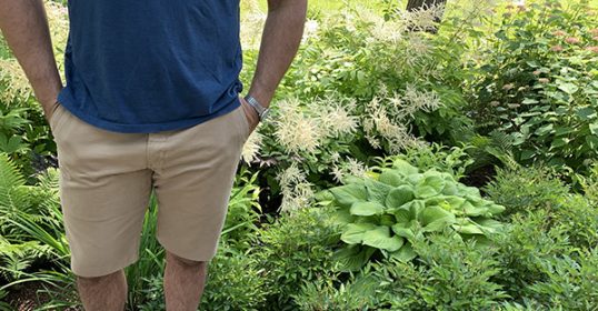 A man standing on a rock in a garden with no pants.