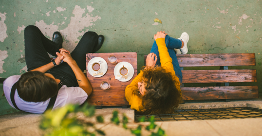 A man and woman sitting on a wooden bench, people enjoying each other's company.