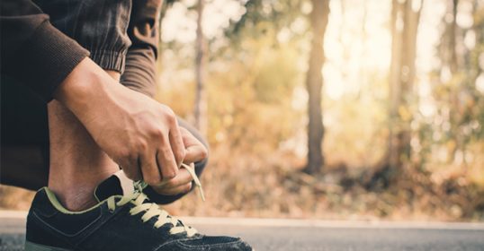 A man tying his shoes on the road, becoming a better man.