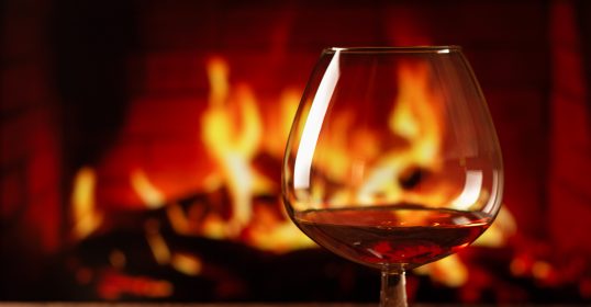 A glass of brandy in front of a fireplace.