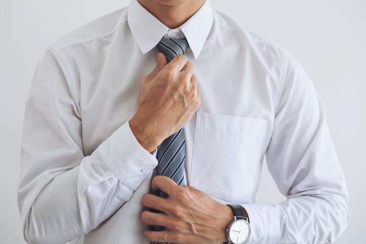 A man is adjusting his tie for work on a white background.