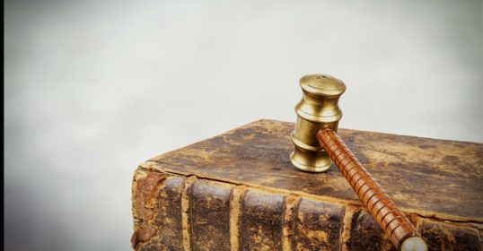 An old book with a gavel on top of it, symbolizing the rules of the universe.