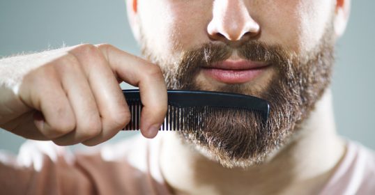 A man is grooming his beard with a comb as part of his routine.