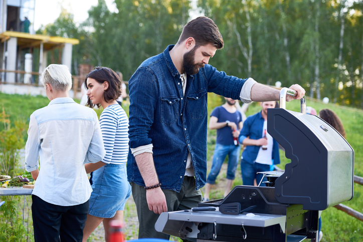 A man grilling while a group of people stands around.