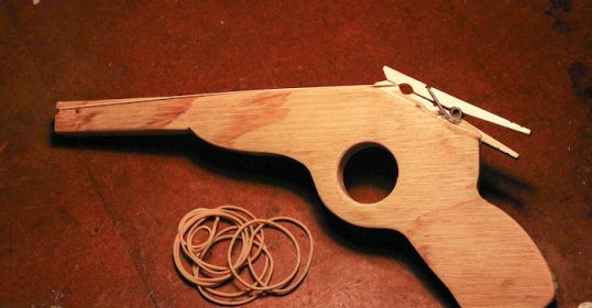 A wooden toy gun sits on a table, perhaps a kid's craft project.