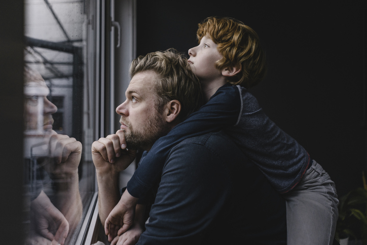 A man and his son looking out a window during the pandemic.